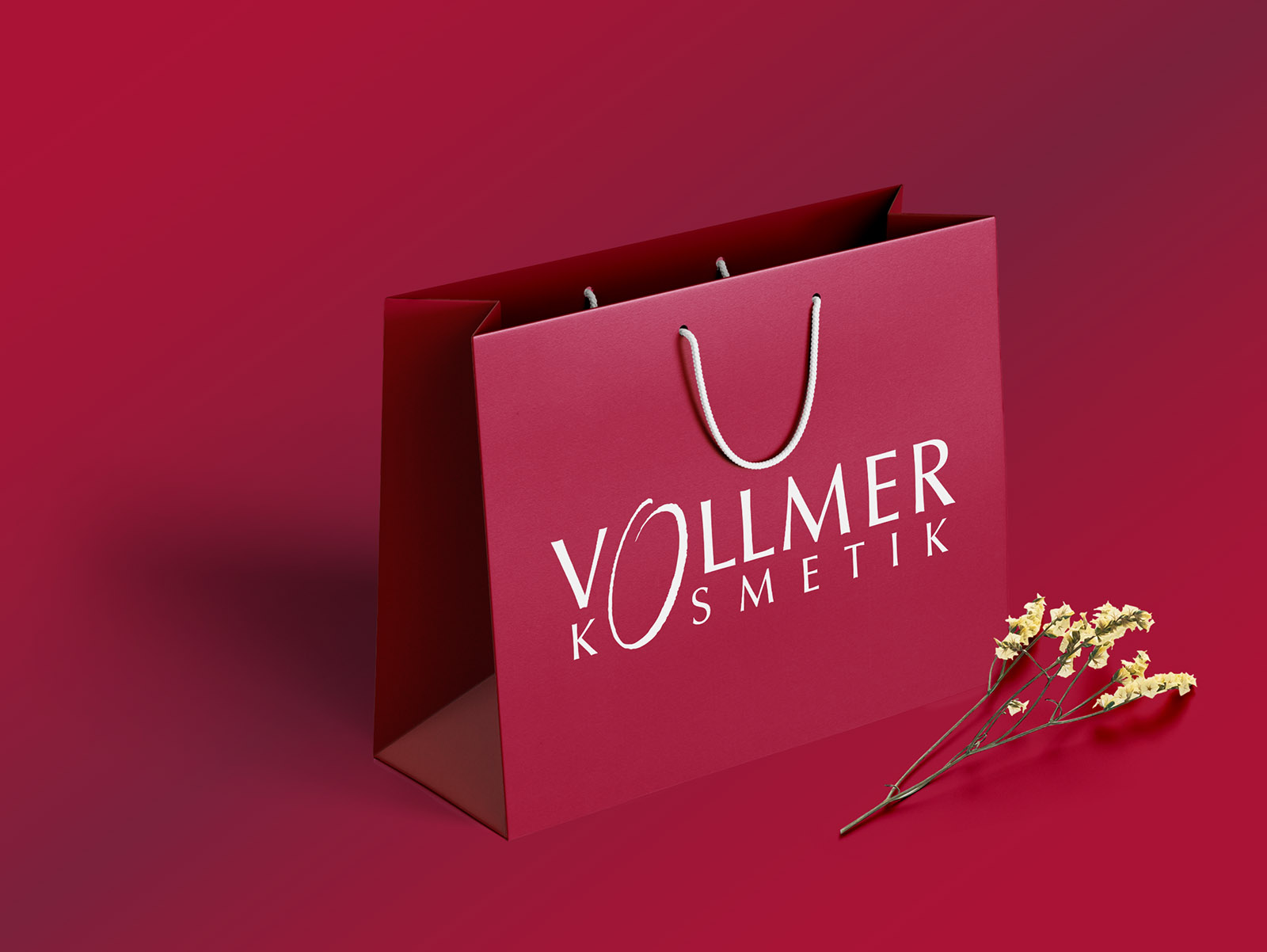 Hochwertige Papiertragetasche mit Vollmer Kosmetik Logo auf weinrotem Hintergrund