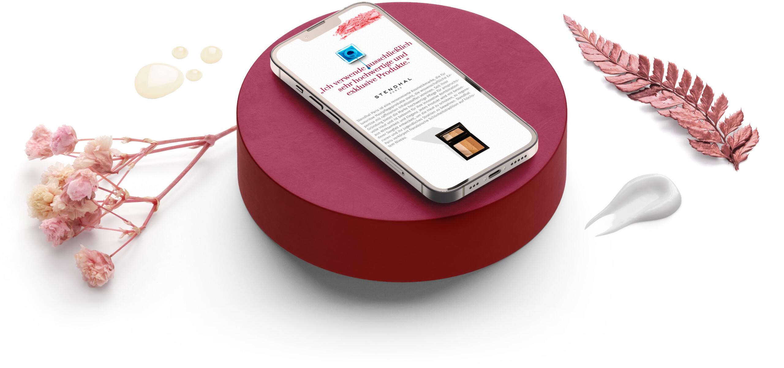 Smartphone mit Vollmer Kosmetik Website auf rundem Sockel in mit Blüten und Blättern dekorierter Umgebung
