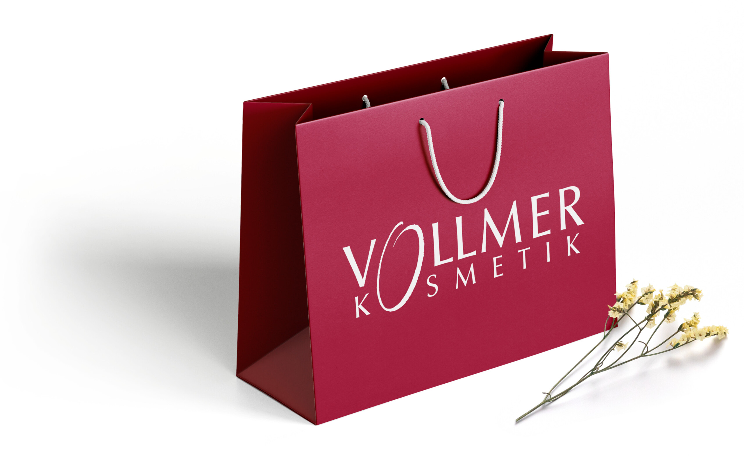 Hochwertige Papiertragetasche mit Vollmer Kosmetik Logo auf weinrotem Hintergrund